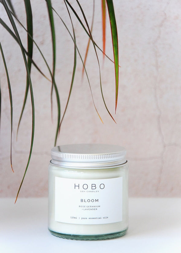 Aromatherapy travel candle, handmade by HoBo Soy Candles using one hundred percent essential oils. The label shows the scent as being rose geranium and lavender. The candle is presented in a one hundred and twenty millilitre recycled clear glass jar with a metal lid. The jar is six centimetres high and five point five centimetres wide.