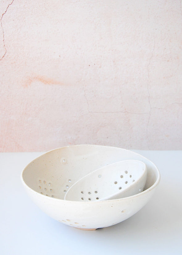 A small berry bowl sitting inside a large berry bowl. Both bowls are ceramic with a white glaze.