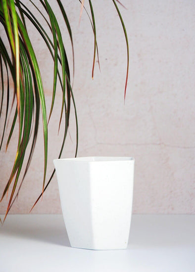 White milk jug, in a geometric design, made from speckled porcelain. Nine point one centimetres tall and eight point three centimetres wide at the top.