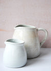 Two jugs, one large with a handle and one small without a handle, both in an ivory colour.