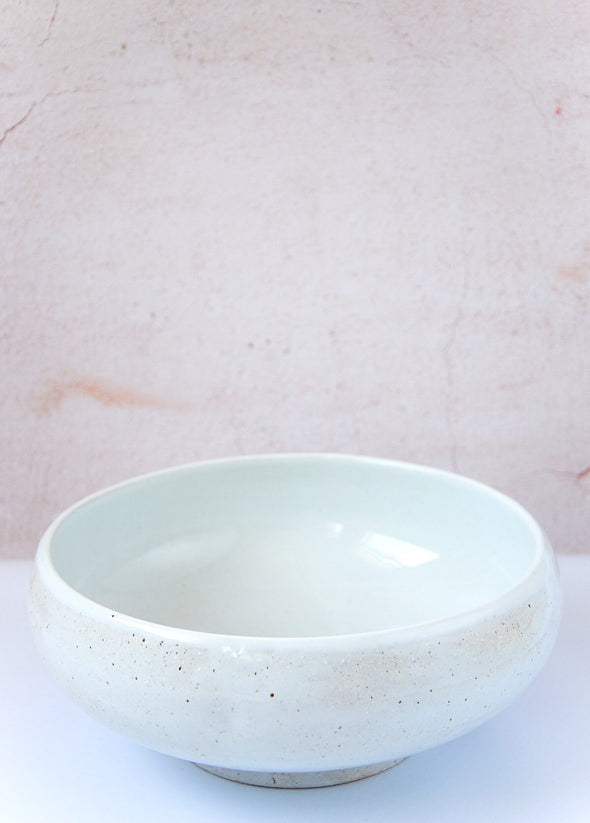 Round serving bowl in a soft ivory colour with a rustic finish. Made from porcelain. Ten centimetres high and twenty-six centimetres wide.