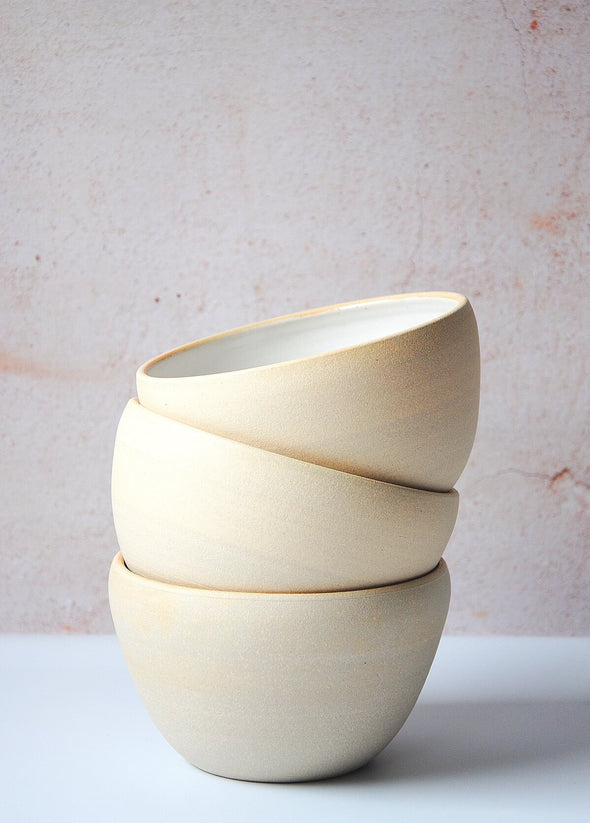 Three bowls stacked on top of each other, handmade by Dor and Tan using local Cornish clay. Each bowl has a white glaze inside and a rustic, natural exterior finish. Each bowl is seven point five centimetres high and fourteen point five centimetres wide.
