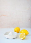 Ceramic citrus squeezer with a white glaze. It is 12cm tall. Resting next to it are two and a half lemons.