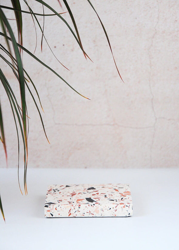 Terrazzo square coaster handmade by Katie Gillies using jesmonite. It has a white base and brown, black and pink chips. It is ten centimetres by ten centimetres.