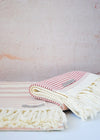A set of two bath towels in cream with rose coloured stripes and cream tassels. Length one hundred and twenty centimetres, width eighty centimetres.