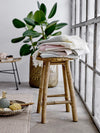 A wooden stool on which is piled a selection of bath towels in grey, rose and green stripes.
