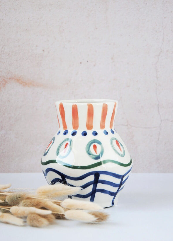 Ceramic vase with a white base and hand painted pattern of bold brush strokes in the colours green, blue and orange. Height fifteen centimetres, width twelve centimetres.