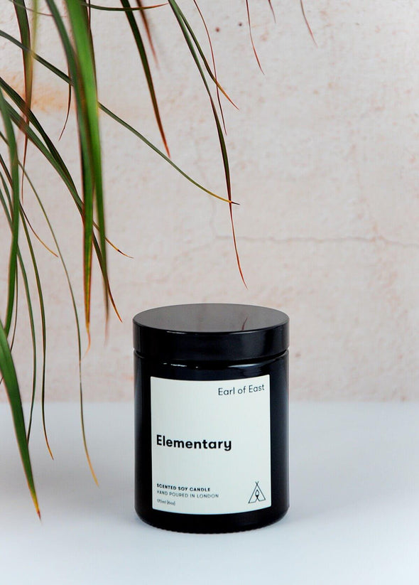 Scented candle in a brown apothecary inspired jar, made by Earl of East London using only natural soy wax. The label shows the name as being Elementary. The jar has a capacity of one hundred and seventy millilitres and is eight centimetres tall and six point five centimetres wide.