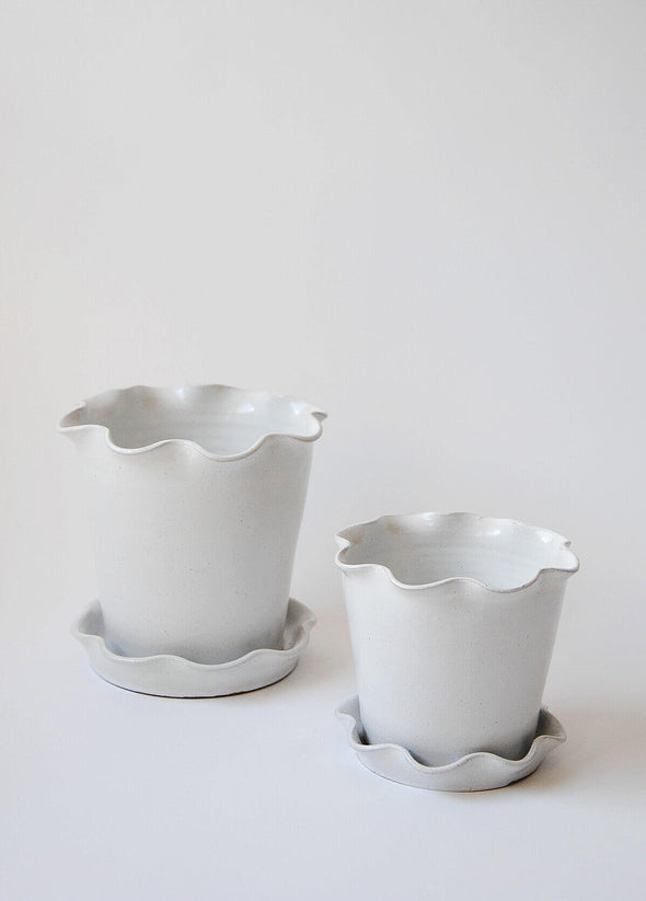 Two stoneware planters and saucers with a white glaze, one large and one small. Both planter and saucer have a frilly edge.
