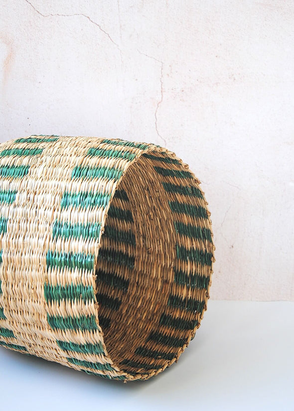 Seagrass basket with green stripes lying on its side. Height thirty one centimetres, width thirty three centimetres.