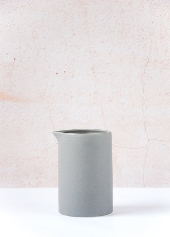 Grey milk jug made of porcelain. Ten centimetres tall and six point five centimetres wide.