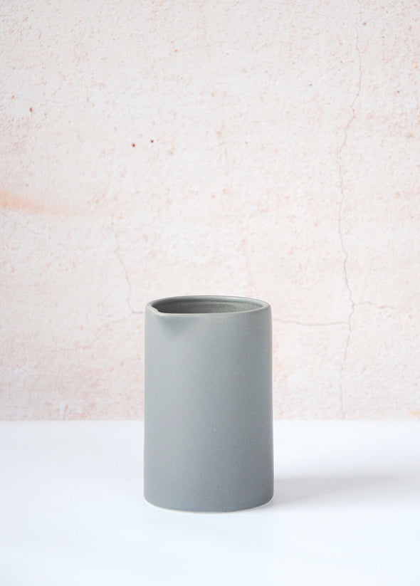 Grey milk jug made of porcelain. Ten centimetres tall and six point five centimetres wide.