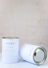 Two scented candles, handmade by Hobo Soy Candles, each packaged in a simple white box. Each box is a white cardboard cylinder with a metal lid and clearly states the respective scent of the candle inside along with other brand details.