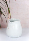 Milk jug in an ivory colour with no handle. Made from porcelain, ten centimetres tall.