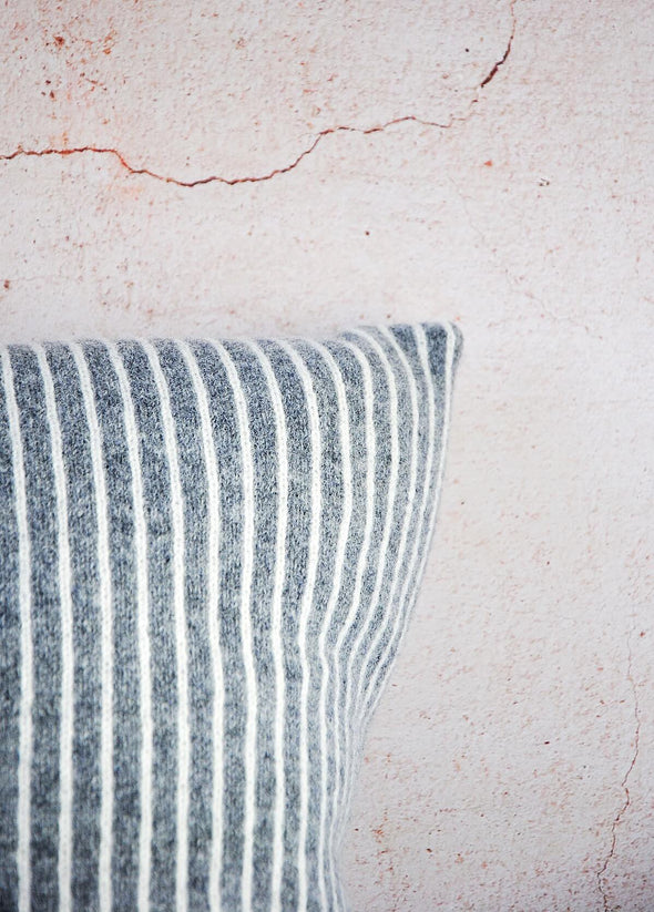 Close up corner of a dark grey knitted lambswool cushion with thin white vertical stripes. Height forty five centimetres, width forty five centimetres.