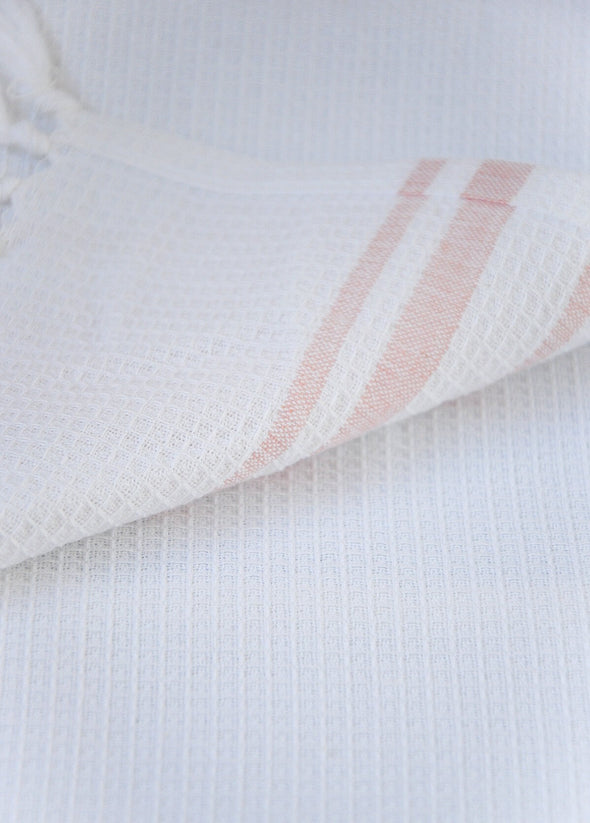 Close up of a kitchen towel in white with rose stripes, showing the waffle texture of the cotton.