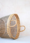 Open weave seagrass basket, lying on its side, in natural and black with handles. Height twenty eight centimetres, width thirty five centimetres.