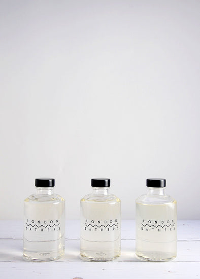 Three glass bottles of foam bath by London Bathers lined up in a row. Each glass bottle has a black plastic cap.