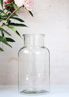 Medium sized clear glass jar vase. Can be used to display flowers. Twenty-five point five centimetres tall and thirteen point five centimetres wide.