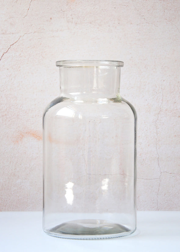 Medium sized clear glass jar vase. Can be used to display flowers. Twenty-five point five centimetres tall and thirteen point five centimetres wide.
