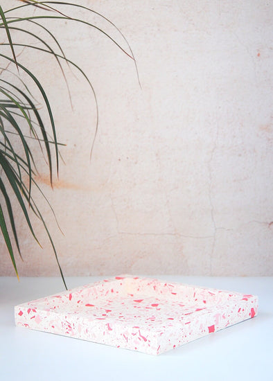 Terrazzo square tray handmade by Katie Gillies using jesmonite. It has a white base and red and pink chips. It is twenty centimetres by twenty centimetres and is two centimetres thick.