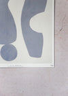 Close up of a corner of a print by Laurie Maun. Depicting a large abstract form in blue on a cream background, with a white border. Numbered by the artist in the corner.