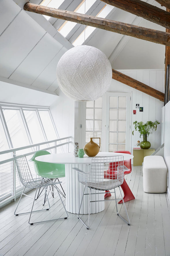 A white and airy room with wooden beams across the top. On a round white table sits a collection of three vases: a small green one, a tall black and white one and a round ceramic mustard coloured one.