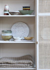Cupboard shelves displaying various ceramic bowls and cups. A blanket is folded on the lower shelf.