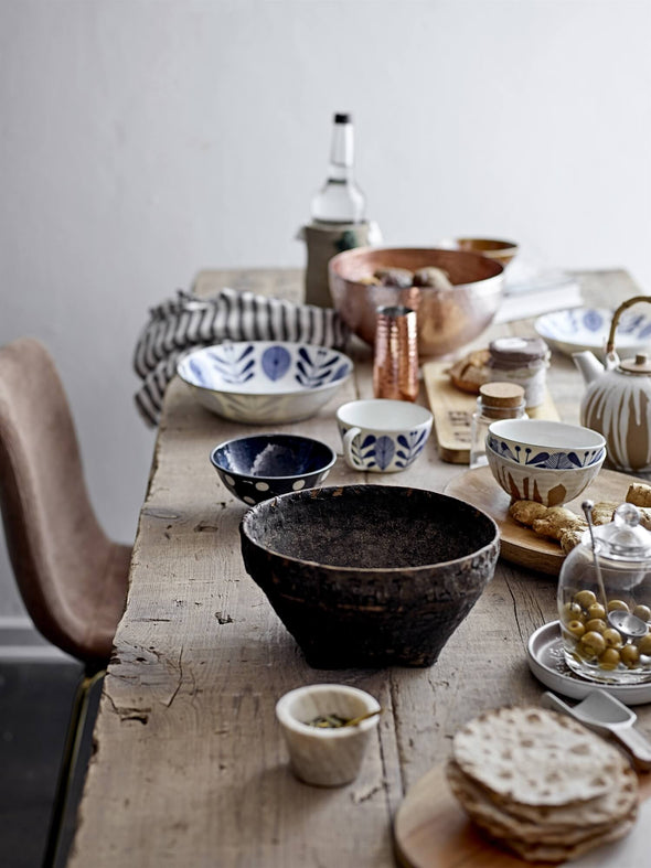 Rustic wooden table with an array of tableware on top, including ceramic and wooden bowls and a brown marble condiment bowl with accompanying brass spoon.