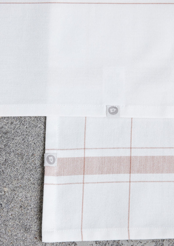 Close up of two kitchen towels. They are white with a nougat stripe and check design.