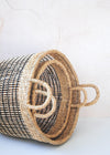 Set of two open weave seagrass baskets, one large and one small, in natural and black. Lying on their side with one nestled inside the other.