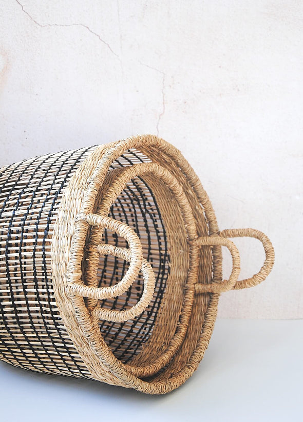 Set of two open weave seagrass baskets, one large and one small, in natural and black. Lying on their side with one nestled inside the other.