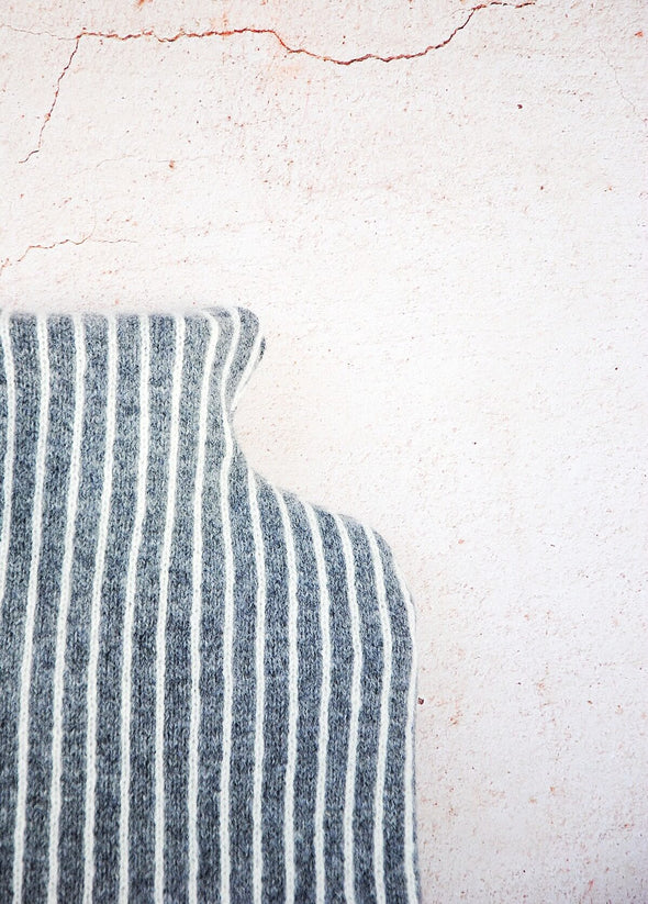 Close up corner of a dark grey knitted lambswool hot water bottle with vertical thin white stripes.