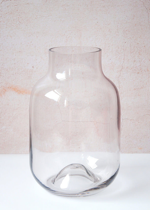 Clear glass vase with a slight hint of delicate aubergine colour to the glass. It has a simple shape and can be used for displaying flowers and foliage. Twenty-five point four centimetres tall and seventeen centimetres wide.