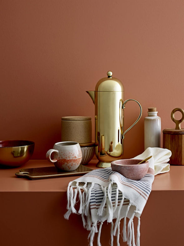 A selection of tableware on a shelf, including a pink marble condiment bowl with brass spoon.