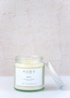 Aromatherapy travel candle, handmade by HoBo Soy Candles using one hundred percent essential oils. The label shows the scent as being bergamot, lavender and patchouli. The candle is presented in a one hundred and twenty millilitre recycled clear glass jar with the metal lid leaning against its side. The jar is six centimetres high and five point five centimetres wide.
