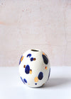Oval shaped porcelain bud vase, handmade by Jade Gallup. Featuring a white glaze base and covered with splodges of deep blue and real gold lustre. Can be used to display one or two stems, or alone as a decorative piece. Approximately eleven centimetres tall.