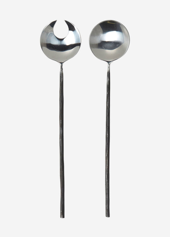 A pair of salad servers made from stainless steel. One has the shape of a spoon and the other the shape of a fork. The handles are long and thin with a darker, rustic finish. Each is thirty centimetres long.