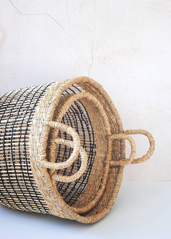 Set of two seagrass baskets in natural and black, one large and one small, lying on their side with one nestled inside the other.