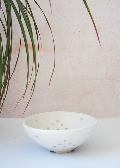 Ceramic berry bowl in a white glaze. A few plant fronds can be seen above the bowl. The bowl is 5.5cm high and 13cm wide at the top.