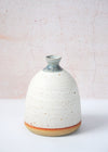 Stoneware dome shaped bud vase, handmade by JG Pottery. Featuring a white glaze on its body with a blue over dip on its neck. Perfect for displaying a single stem. Fourteen centimetres tall and eleven centimetres wide at its base.