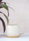 Stoneware mug handmade by JG Pottery, with a white glaze and rustic finish. Eight centimetres tall and thirteen point five centimetres wide including the handle.