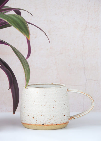 Stoneware mug handmade by JG Pottery, with a white glaze and rustic finish. Eight centimetres tall and thirteen point five centimetres wide including the handle.