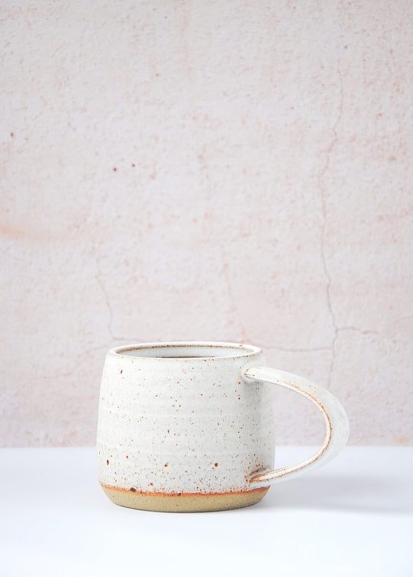 Stoneware mug handmade by JG Pottery, with a white glaze and rustic finish. Eight centimetres tall and thirteen point five centimetres wide including the handle.