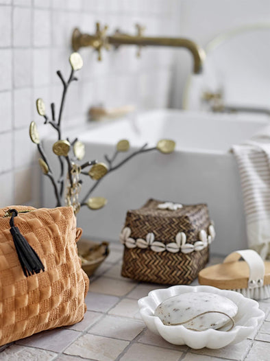 Collection of bathroom products on a tiled surface next to a sink. Including a wash bag and a white marble fluted dish containing a round hand soap.