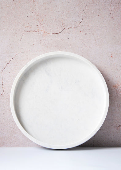 Round white marble tray leaning upright against a wall.