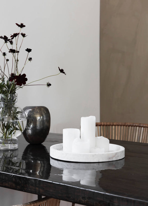 Round white marble tray on a black table. A few pillar candles sit on the tray, and two vases are displayed next to it.
