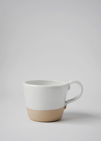 A stoneware mug finished in a glossy white glaze, the bottom third is left raw.