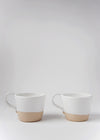 Two stoneware mugs sitting side by side. They are finished in a glossy white glaze, the bottom third is left raw.