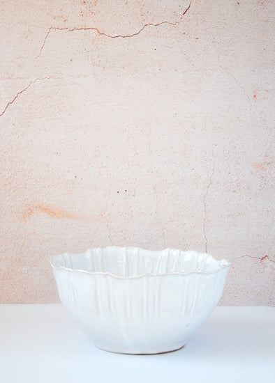 Bowl with fluted edges in a white glaze. Made from terracotta. Nine centimetres high and twenty centimetres wide.